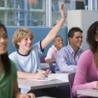 Close-up af unge i et klasselokale - en rækker en hånd i vejret