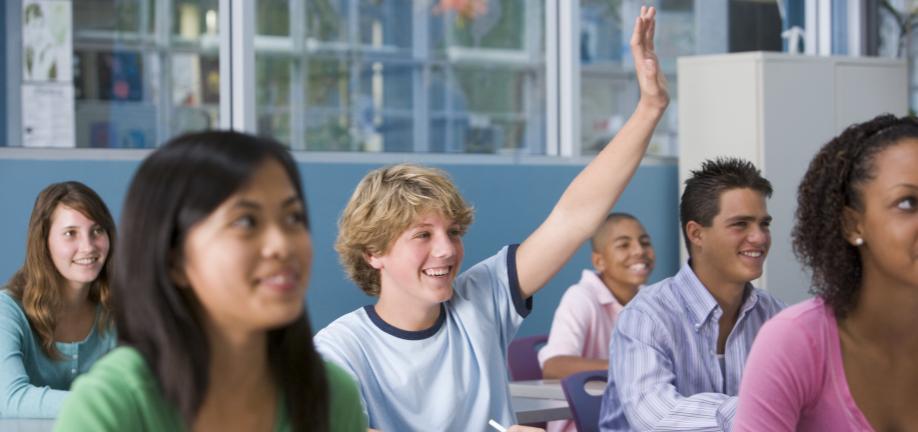 Close-up af unge i et klasselokale - en rækker en hånd i vejret